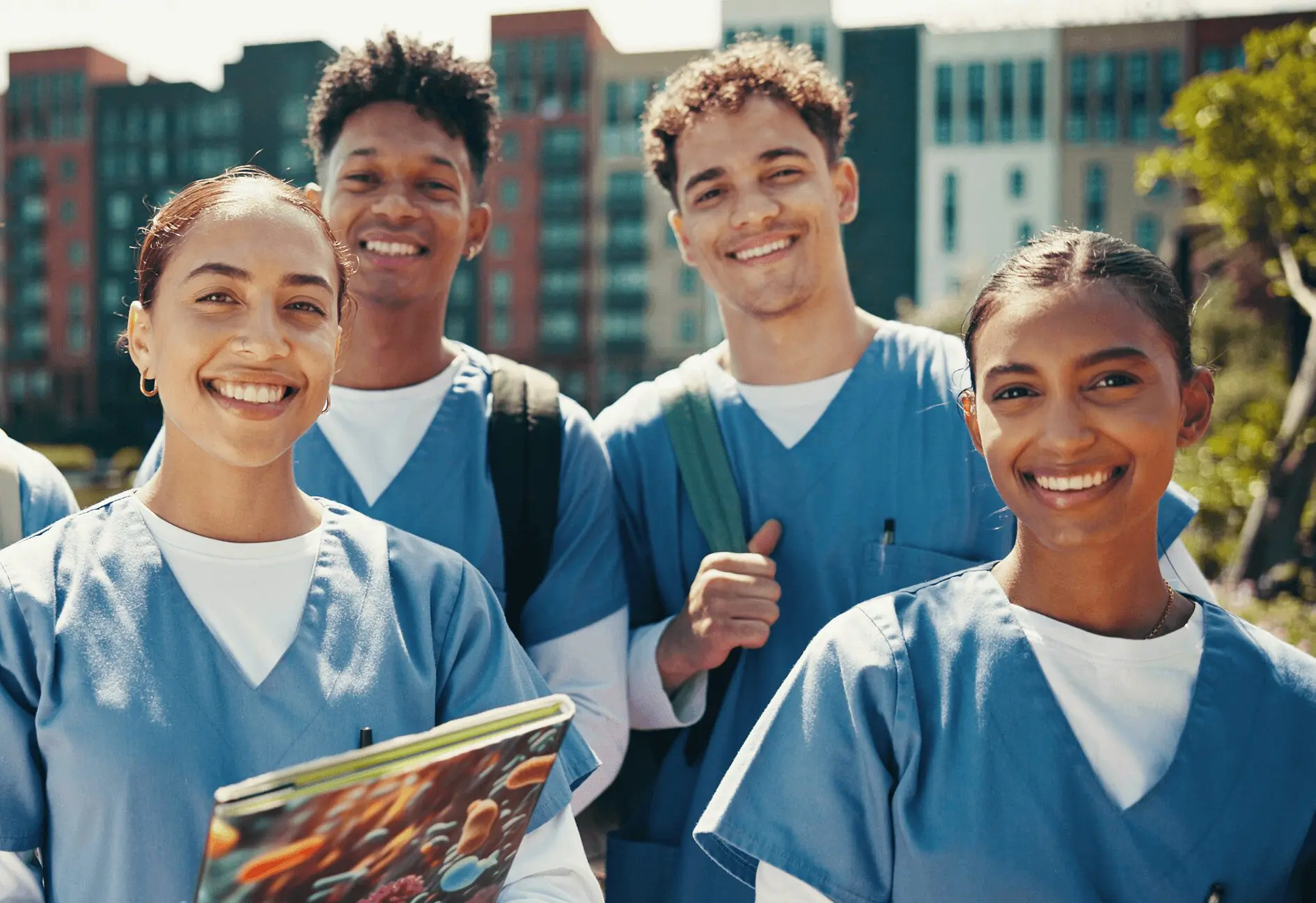h2 Medical students smiling outdoors, wearing scrubs.